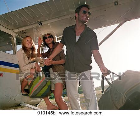 Stock Image - one man and two women posing like fashion models near small propeller plane. Fotosearch