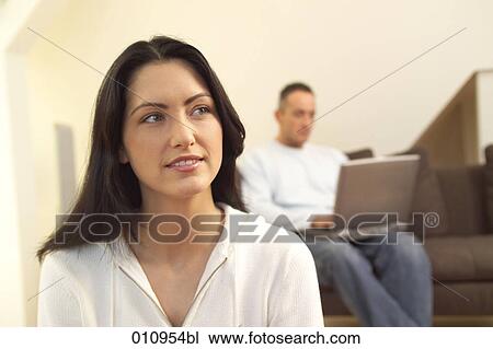 Stock Image - Portrait of pensive looking young woman while her friend is working on a computer . Fotosearch