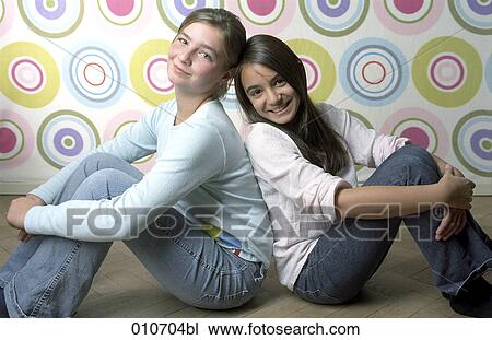 Stock Image - portrait of two smiling girls sitting back to back. Fotosearch