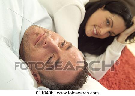 Stock Image - Portrait of young couple, woman facing camera while man is dozing. Fotosearch