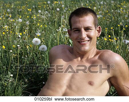 Stock Image - portrait of young man (20-25 years) lying in the grass. Fotosearch