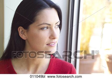 Stock Image - Portrait of young woman looking out of window. Fotosearch