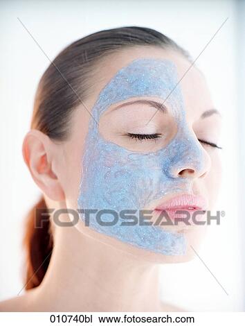 Stock Image - portrait of young woman with one face side covered by mud mask. Fotosearch