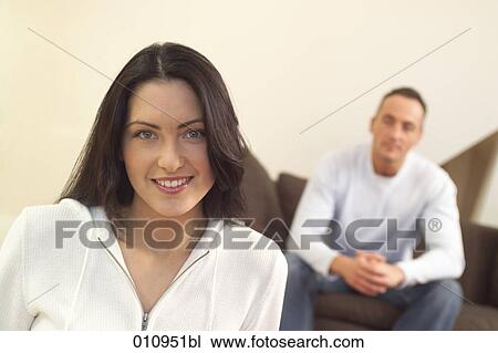 Stock Image - Portrait of young woman with partner sitting in the background. Fotosearch