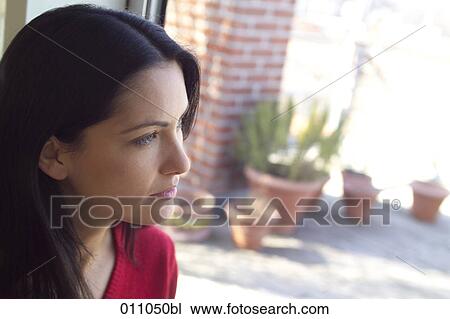 Stock Image - Profile of young woman looking out of window. Fotosearch