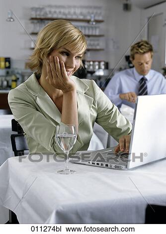 Stock Image - smiling businesswoman looking at computer screen in restaurant. Fotosearch