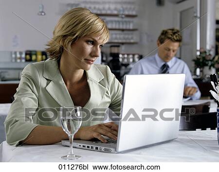 Stock Image - smiling businesswoman looking at computer screen in restaurant. Fotosearch