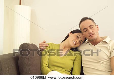 Stock Image - Smiling woman on sofa embraced by her partner . Fotosearch
