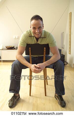 Stock Image - Smiling young man sitting on chair. Fotosearch