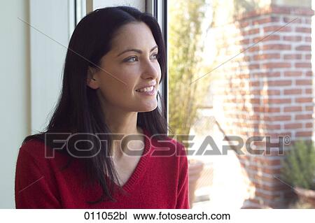 Smiling young woman looking out of window View Large Photo Image Stock Image - Smiling young woman looking out of window. Fotosearch