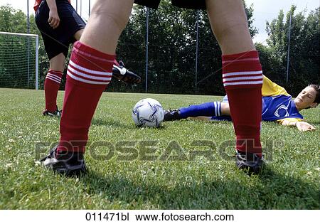 Stock Image - teenage footballer trying to pass the ball while lying on the ground. Fotosearch