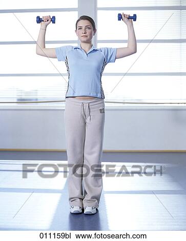 Stock Image - Teenage girl doing exercises with little dumb bells. Fotosearch