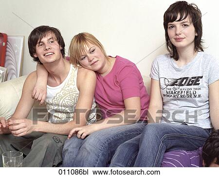 Stock Image - Teenage girl embracing her boyfriend while sitting with others on a couch. Fotosearch