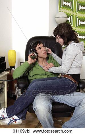 Stock Image - Teenage girl sitting on lap of boyfriend who is listening to music. Fotosearch