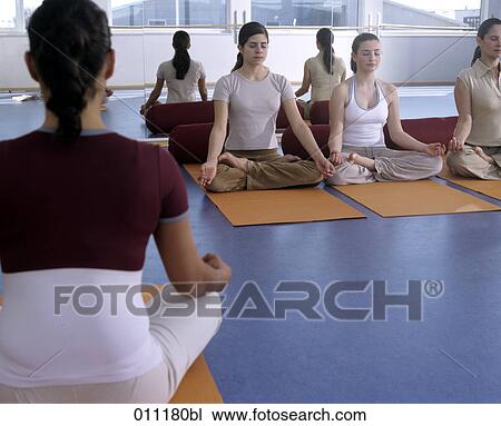 Stock Image - Three teenage girls sitting in lotus position overviewed by instructor. Fotosearch