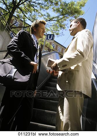 two businessmen having a conversation on the escalator of an underground station View Large Photo Image Stock Image - two businessmen having a conversation on the escalator of an underground station. Fotosearch