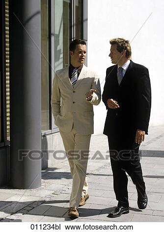 Stock Image - two businessmen having a conversation while walking together. Fotosearch