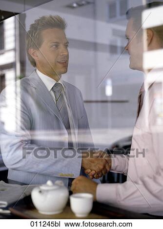 Stock Image - two businessmen meeting in a cafe seen through window. Fotosearch