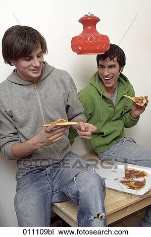 Stock Image - Two friends sitting on a table and having pizza together. Fotosearch