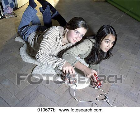 Stock Image - two girls lying on the floor playing computer games. Fotosearch