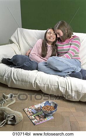 two girls sitting on a sofa and sharing a laugh View Large Photo Image Stock Image - two girls sitting on a sofa and sharing a laugh. Fotosearch