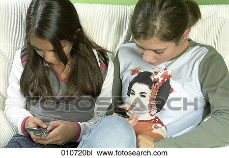 two girls sitting together writing text messages on mobile phones View Large Photo Image Stock Image - two girls sitting together writing text messages on mobile phones. Fotosearch