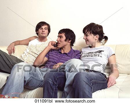 Stock Image - Two teenagers watching friend as he is talking on mobile phone. Fotosearch