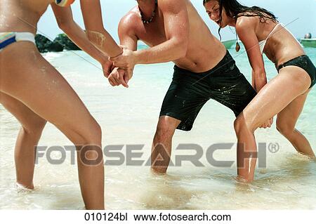 Stock Image - two women and one man playing on the beach. Fotosearch
