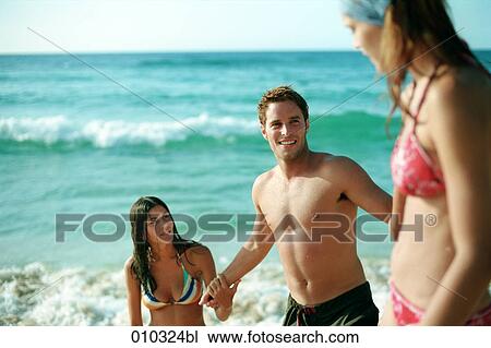 Stock Image - two women and one man playing on the beach. Fotosearch