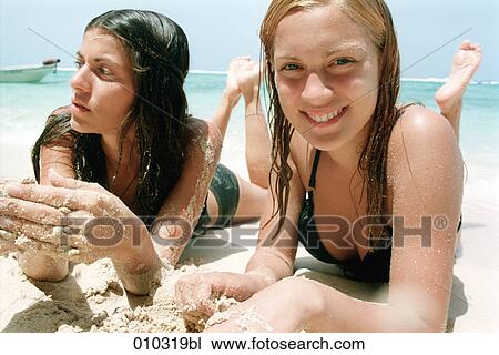 Stock Image - two young women lying in the sand at the beach relaxing. Fotosearch