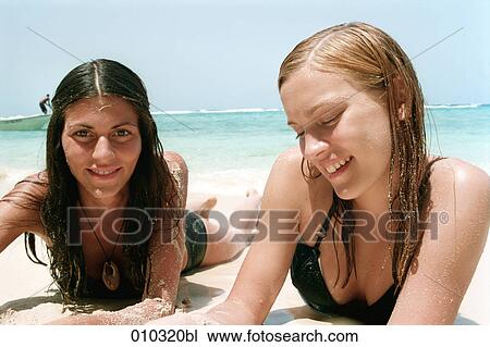Stock Image - two young women lying in the sand at the beach relaxing and talking. Fotosearch