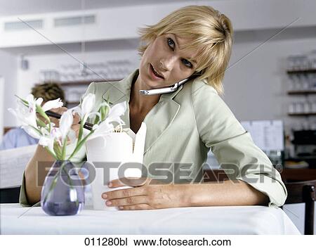 Stock Image - woman eating with chopsticks while talking on mobile. Fotosearch