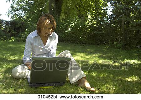 Stock Image - woman in her garden working with her laptop computer. Fotosearch