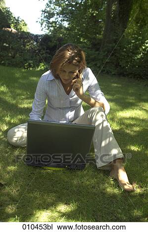 Stock Image - woman in her garden working with her laptop computer. Fotosearch