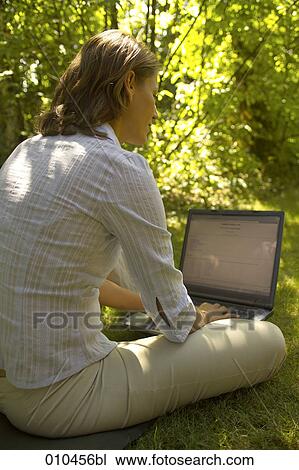 Stock Image - woman in her garden working with her laptop computer. Fotosearch
