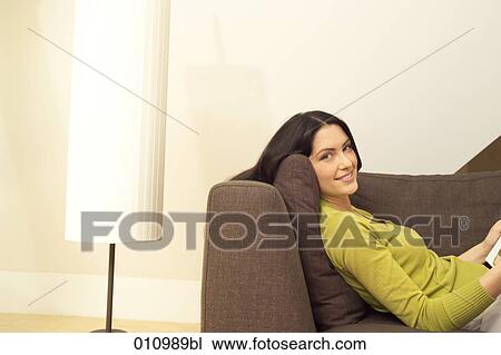 Stock Image - Woman lying on sofa facing camera. Fotosearch
