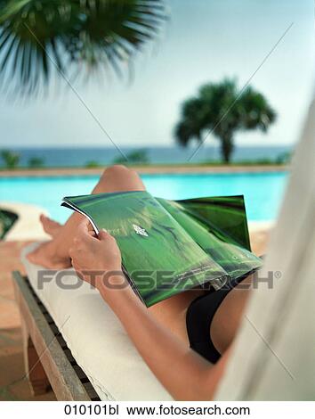 Stock Image - woman on deck chair sunbathing and reading a magazine. Fotosearch