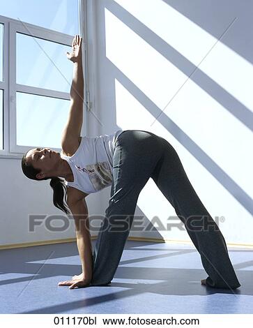 Stock Image - Woman performing the triangle pose in gym. Fotosearch
