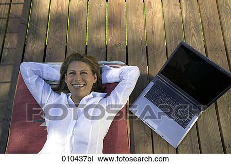 Stock Image - woman relaxing on her veranda, laptop beside her. Fotosearch