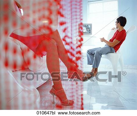 Stock Image - woman sitting on a sofa, while boyfriend is watching tv. Fotosearch