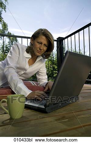 Stock Image - woman working with laptop on her veranda at home. Fotosearch