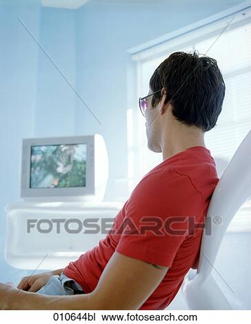 Stock Image - yong man in red t-shirt watching tv. Fotosearch