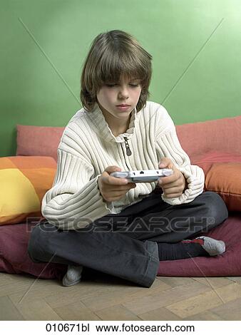 Stock Image - young boy sitting cross-legged and playing with gameboy. Fotosearch