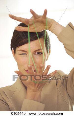 Stock Image - young businesswoman looking through the green thread while doing the cat´s cradle . Fotosearch