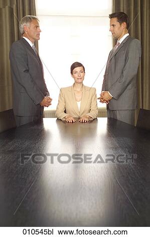young businesswoman sitting at desk surrounded by two businessmen View Large Photo Image Stock Image - young businesswoman sitting at desk surrounded by two businessmen. Fotosearch