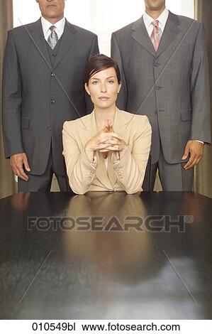 young businesswoman sitting at table with two businessmen standing in the background View Large Photo Image Stock Image - young businesswoman sitting at table with two businessmen standing in the background. Fotosearch