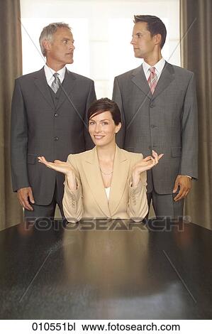 young businesswoman sitting at table while two businessmen behind her look on View Large Photo Image Stock Image - young businesswoman sitting at table while two businessmen behind her look on. Fotosearch