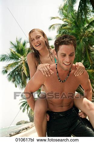 Stock Image - young couple enjoying a piggyback ride on a tropical beach. Fotosearch