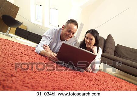 Stock Image - Young couple lying on the floor working with laptop computer. Fotosearch