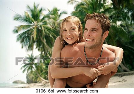 Stock Image - young man giving his girlfriend a piggyback ride on the beach. Fotosearch